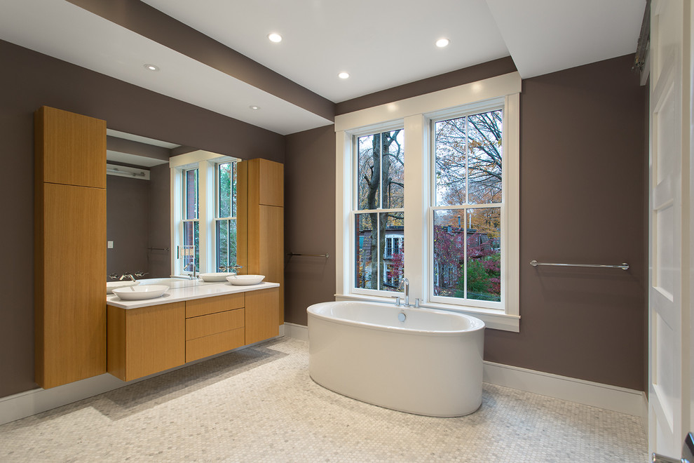 Design ideas for a mid-sized modern master bathroom in Boston with flat-panel cabinets, medium wood cabinets, a freestanding tub, gray tile, white tile, ceramic tile, grey walls, ceramic floors, a vessel sink and solid surface benchtops.