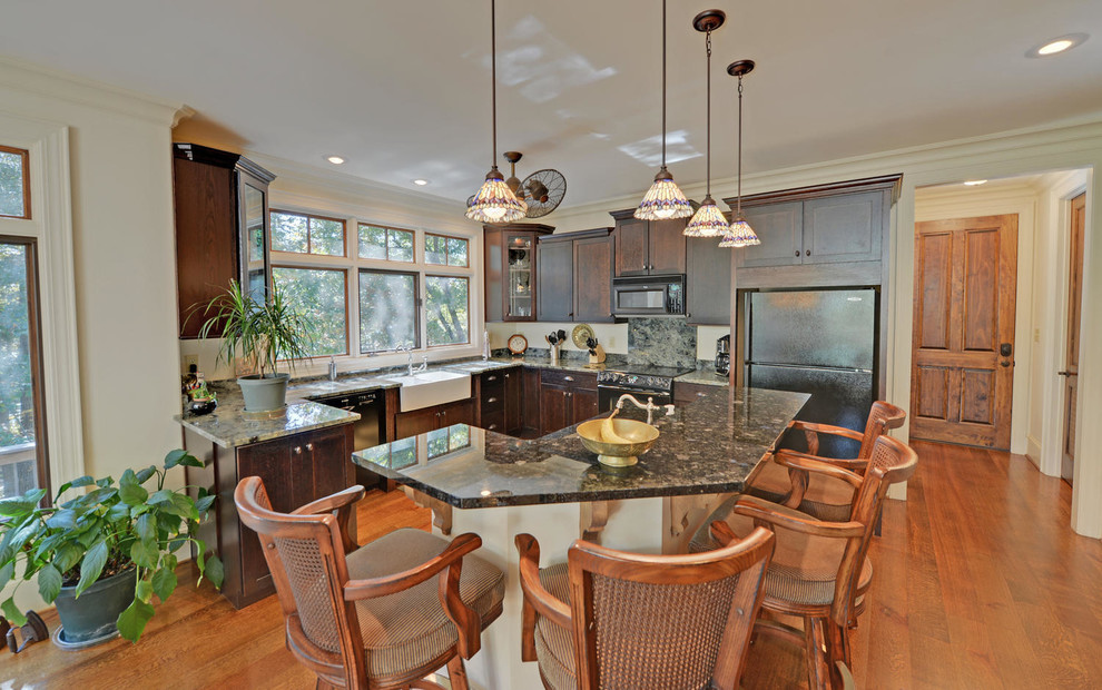 This is an example of a large arts and crafts l-shaped eat-in kitchen in Atlanta with a farmhouse sink, shaker cabinets, dark wood cabinets, granite benchtops, multi-coloured splashback, stone slab splashback, black appliances, medium hardwood floors, with island, brown floor and multi-coloured benchtop.