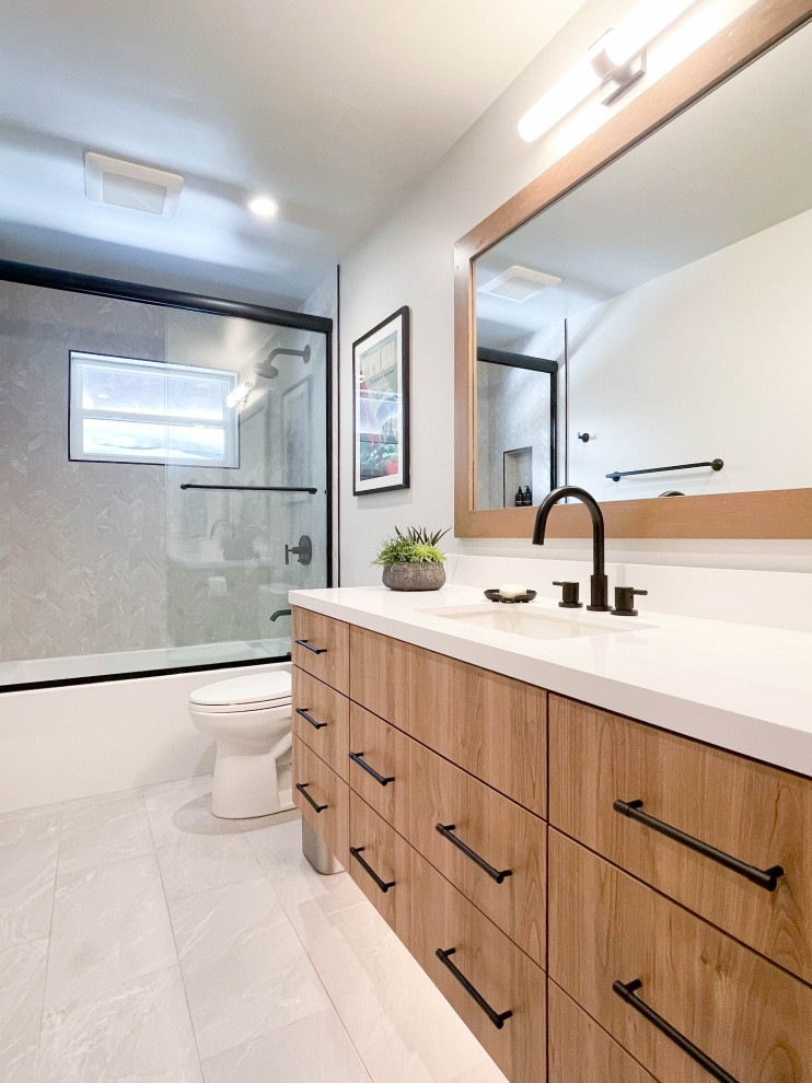 Photo of a mid-sized contemporary kids bathroom in Sacramento with flat-panel cabinets, brown cabinets, an alcove tub, a shower/bathtub combo, a one-piece toilet, gray tile, porcelain tile, grey walls, ceramic floors, an undermount sink, engineered quartz benchtops, grey floor, a sliding shower screen, white benchtops, a niche, a single vanity and a built-in vanity.