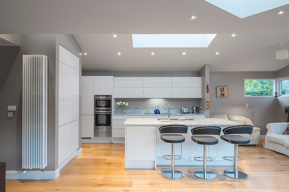 Photo of a contemporary kitchen in Dublin with an undermount sink, flat-panel cabinets, white cabinets, grey splashback, stainless steel appliances, light hardwood floors and with island.