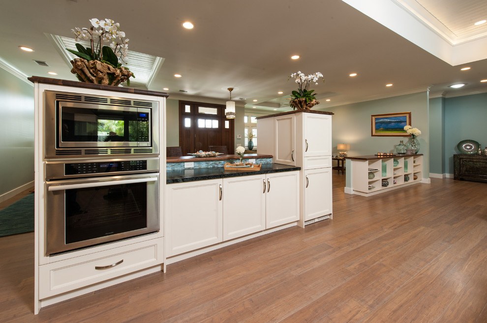 Design ideas for a large transitional l-shaped open plan kitchen in Hawaii with an undermount sink, shaker cabinets, white cabinets, soapstone benchtops, blue splashback, glass sheet splashback, panelled appliances, bamboo floors and with island.