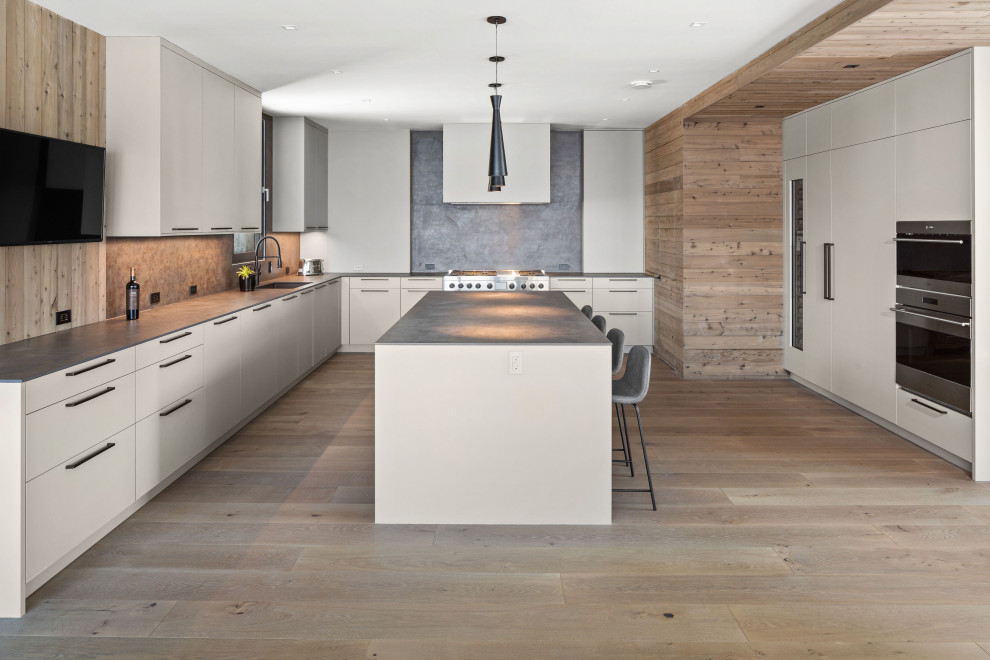 Large modern l-shaped kitchen/diner in New York with flat-panel cabinets, white cabinets, grey splashback, an island and grey worktops.