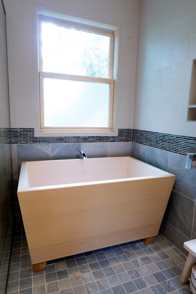 Photo of a mid-sized asian master bathroom in Portland with flat-panel cabinets, light wood cabinets, a freestanding tub, a corner shower, a two-piece toilet, gray tile, slate, white walls, porcelain floors, an undermount sink, engineered quartz benchtops, grey floor, a hinged shower door and white benchtops.