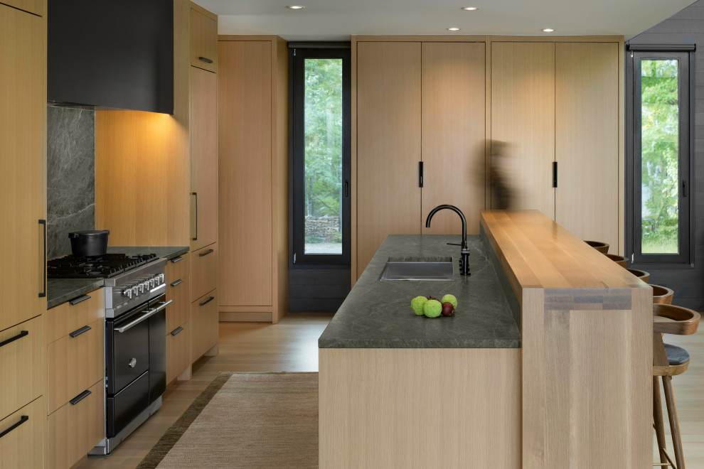 Bild på ett stort funkis grön grönt kök, med en undermonterad diskho, släta luckor, skåp i mellenmörkt trä, bänkskiva i kvartsit, grönt stänkskydd, stänkskydd i sten, rostfria vitvaror, ljust trägolv, en köksö och brunt golv