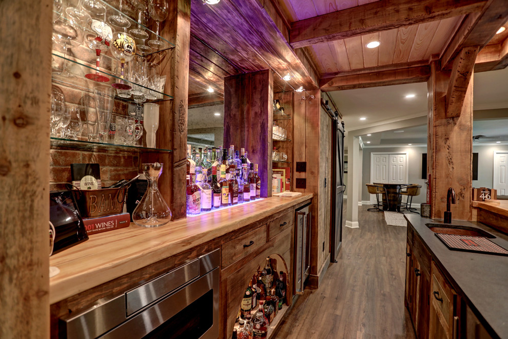 Large country galley seated home bar in Atlanta with an undermount sink, flat-panel cabinets, medium wood cabinets, wood benchtops, brick splashback, laminate floors, brown floor and grey benchtop.