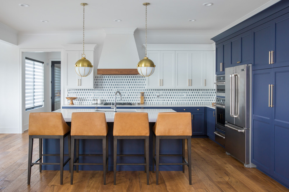 Photo of a beach style l-shaped kitchen in Indianapolis with an undermount sink, shaker cabinets, blue cabinets, multi-coloured splashback, stainless steel appliances, medium hardwood floors, with island, brown floor and white benchtop.