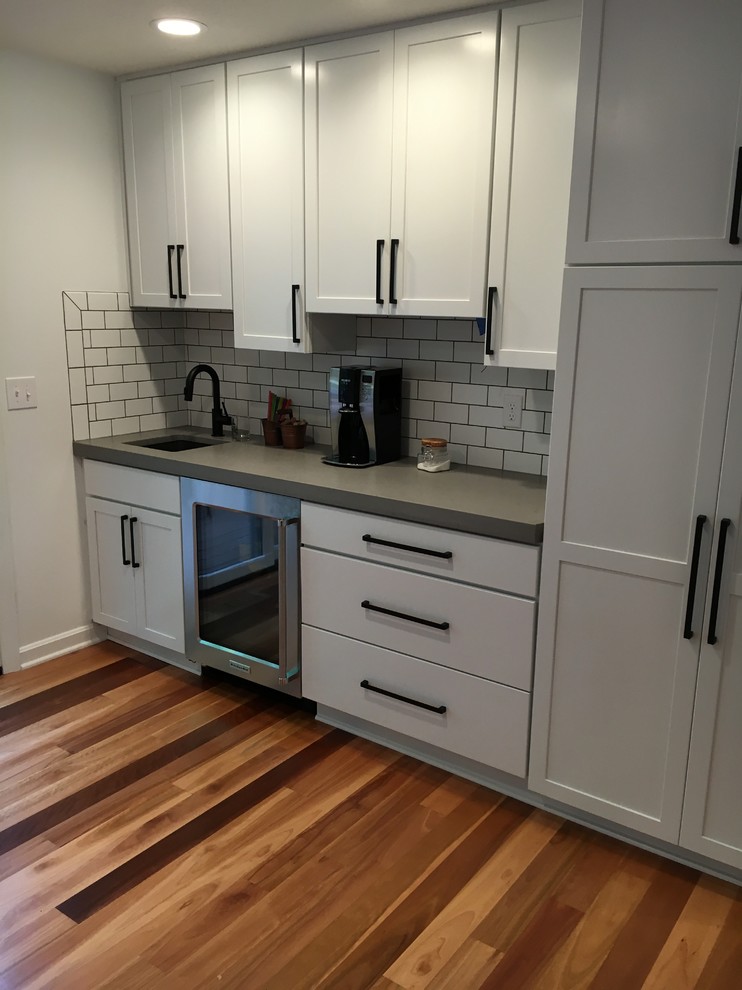 Large contemporary u-shaped open plan kitchen in Columbus with an undermount sink, recessed-panel cabinets, white cabinets, quartz benchtops, white splashback, ceramic splashback, stainless steel appliances, light hardwood floors and no island.