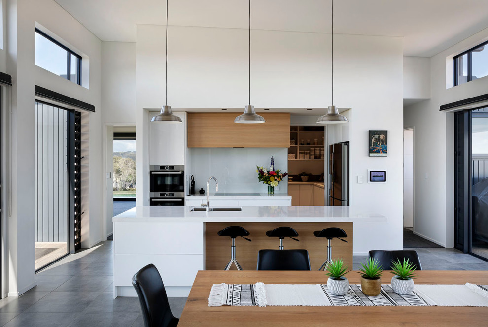 Foto på ett mellanstort funkis vit linjärt kök och matrum, med en undermonterad diskho, luckor med infälld panel, vita skåp, bänkskiva i terrazo, grått stänkskydd, glaspanel som stänkskydd, rostfria vitvaror, cementgolv, en köksö och grått golv