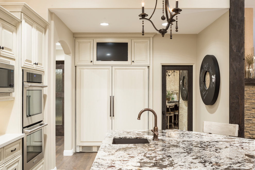 Eat-in kitchen - large transitional l-shaped medium tone wood floor and brown floor eat-in kitchen idea in Phoenix with an undermount sink, raised-panel cabinets, beige cabinets, quartz countertops, beige backsplash, glass tile backsplash, stainless steel appliances and an island