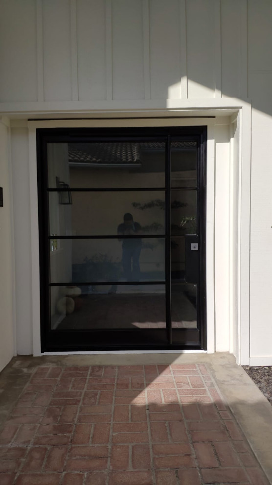This is an example of a medium sized contemporary front door in Orange County with white walls, brick flooring, a pivot front door, a black front door and red floors.