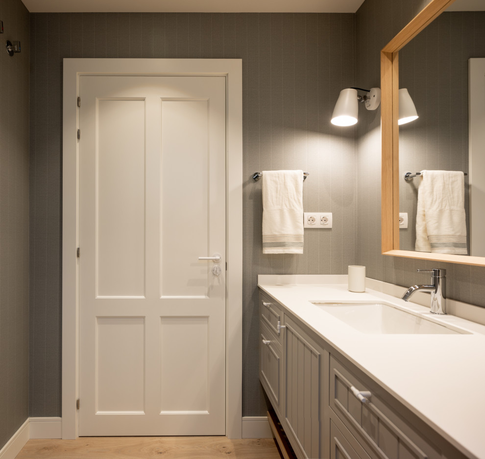 Exempel på ett stort klassiskt vit vitt badrum för barn, med luckor med upphöjd panel, vita skåp, en kantlös dusch, en vägghängd toalettstol, grå kakel, grå väggar, laminatgolv, ett undermonterad handfat, bänkskiva i kvarts och dusch med skjutdörr