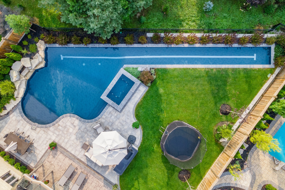 Photo of a large transitional backyard custom-shaped lap pool in Toronto with with a pool and natural stone pavers.