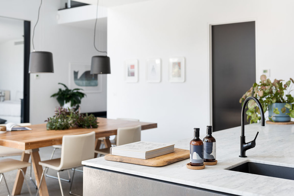 Inspiration for a mid-sized modern galley open plan kitchen in Melbourne with a single-bowl sink, flat-panel cabinets, black cabinets, marble benchtops, grey splashback, marble splashback, black appliances, concrete floors, with island, grey floor and grey benchtop.