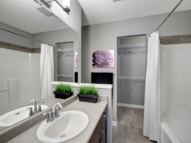 Photo of a mid-sized traditional master bathroom in Edmonton with a console sink, flat-panel cabinets, medium wood cabinets, laminate benchtops, an alcove tub, an alcove shower, a one-piece toilet, brown tile, ceramic tile, grey walls and ceramic floors.