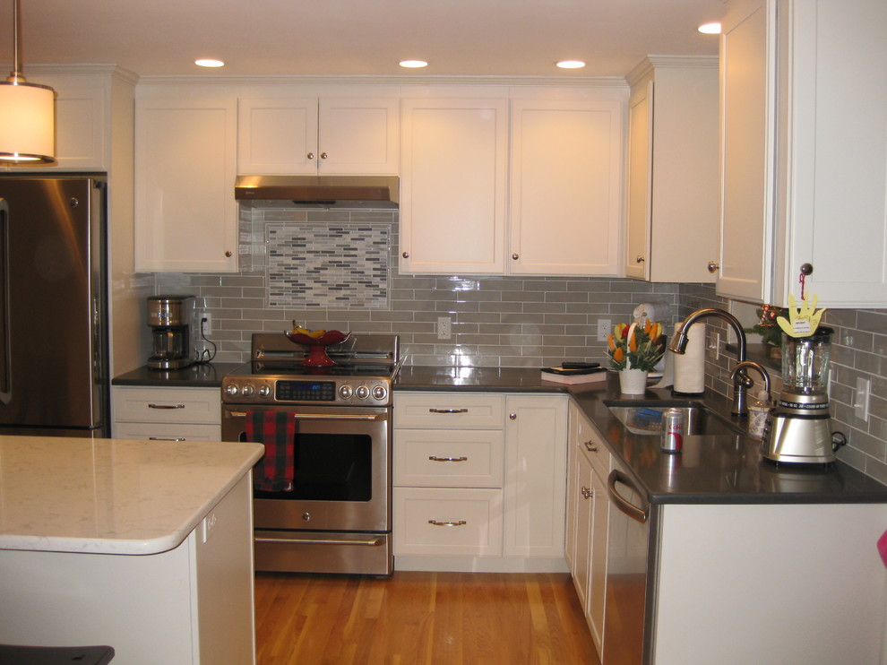 Transitional l-shaped medium tone wood floor eat-in kitchen photo in Boston with an undermount sink, white cabinets, quartz countertops, stainless steel appliances, an island, shaker cabinets, green backsplash, subway tile backsplash and black countertops