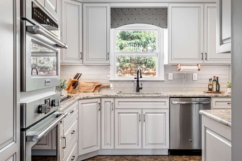 Inspiration for a mid-sized l-shaped eat-in kitchen in Other with a double-bowl sink, raised-panel cabinets, white cabinets, granite benchtops, grey splashback, glass tile splashback, stainless steel appliances, ceramic floors, no island, brown floor and beige benchtop.