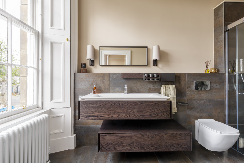 Foto på ett vintage badrum, med släta luckor, skåp i mörkt trä, brun kakel, beige väggar, brunt golv, en kantlös dusch, en vägghängd toalettstol, kakel i metall, ett väggmonterat handfat och dusch med skjutdörr
