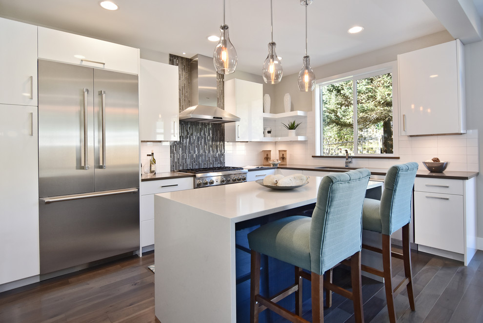 Photo of a contemporary l-shaped open plan kitchen in Seattle with an undermount sink, flat-panel cabinets, white cabinets, white splashback, stainless steel appliances, dark hardwood floors and with island.