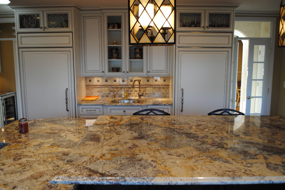 Example of a mid-sized l-shaped medium tone wood floor enclosed kitchen design with a double-bowl sink, raised-panel cabinets, white cabinets, granite countertops, beige backsplash, stone tile backsplash, stainless steel appliances and an island