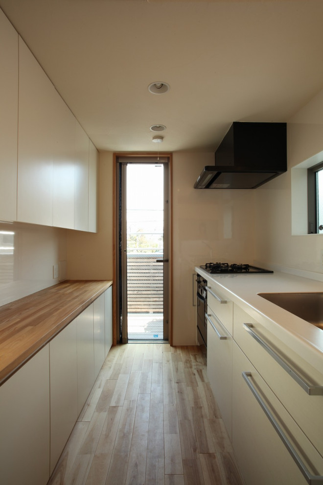 Mid-sized modern single-wall open plan kitchen in Tokyo with an undermount sink, beaded inset cabinets, white cabinets, solid surface benchtops, white splashback, medium hardwood floors, with island, brown floor, white benchtop and black appliances.