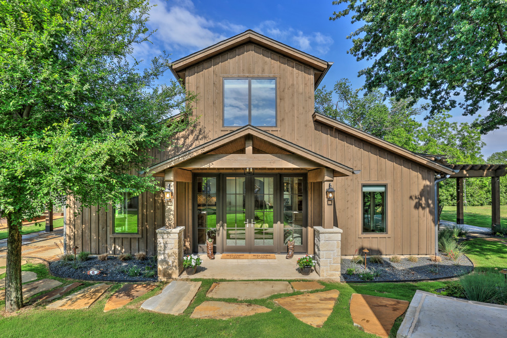 This is an example of an expansive country two-storey stucco brown exterior in Dallas with a gable roof, a shingle roof, a grey roof and board and batten siding.