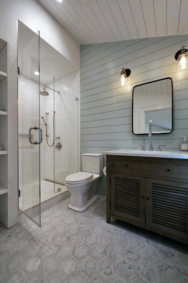 Mid-sized country bathroom in Boston with louvered cabinets, medium wood cabinets, an alcove shower, a two-piece toilet, white tile, ceramic tile, blue walls, marble floors, an undermount sink, marble benchtops, grey floor, a hinged shower door and white benchtops.