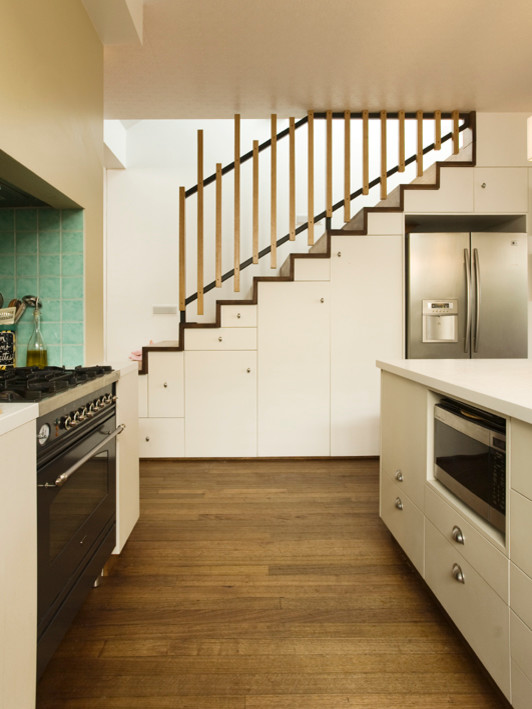 Exempel på ett mellanstort vit vitt kök, med släta luckor, beige skåp, bänkskiva i kvarts, grönt stänkskydd, stänkskydd i keramik, svarta vitvaror, mellanmörkt trägolv, en köksö och brunt golv