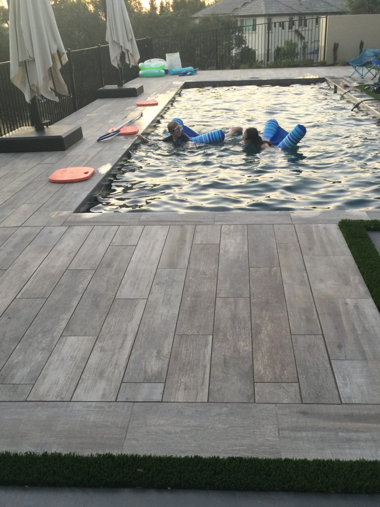 Diseño de piscina clásica renovada grande rectangular en patio trasero con paisajismo de piscina y losas de hormigón
