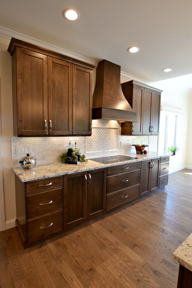 This is an example of a traditional l-shaped open plan kitchen in Denver with an undermount sink, shaker cabinets, dark wood cabinets, stainless steel appliances, medium hardwood floors and with island.