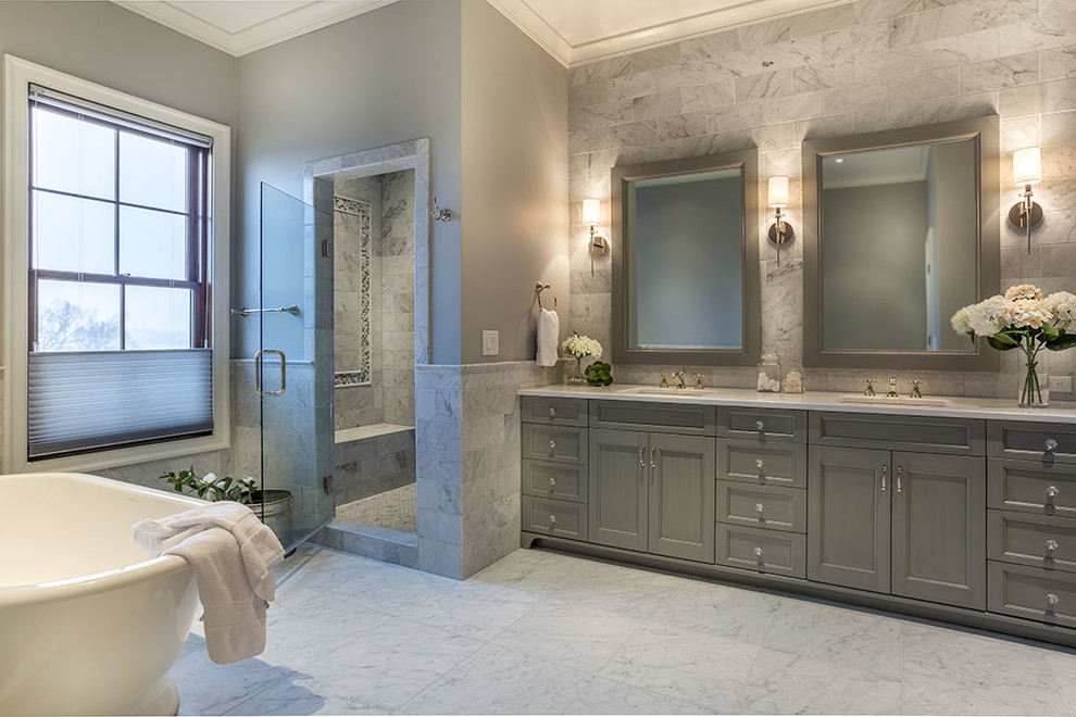 This is an example of a large transitional master bathroom in Other with recessed-panel cabinets, grey cabinets, a freestanding tub, an alcove shower, gray tile, white tile, stone tile, grey walls, marble floors, an undermount sink and solid surface benchtops.