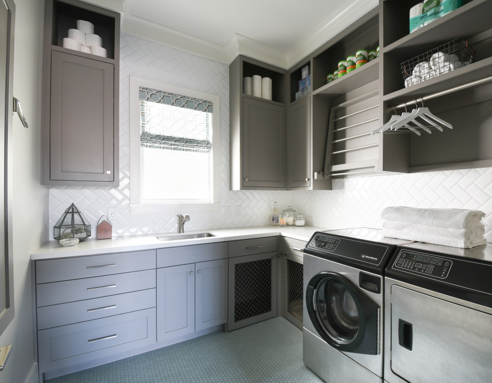 Inspiration for a large transitional l-shaped dedicated laundry room in Houston with an undermount sink, shaker cabinets, grey cabinets, white splashback, a side-by-side washer and dryer, grey floor and white benchtop.