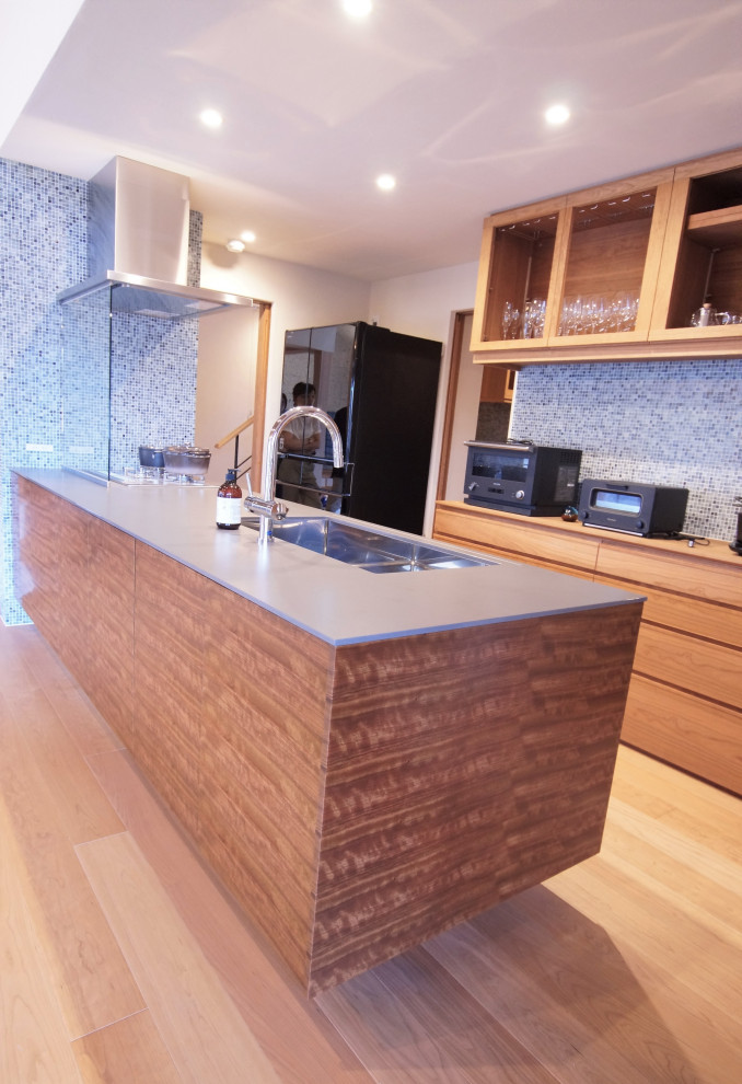 Photo of a large asian single-wall open plan kitchen in Other with an undermount sink, solid surface benchtops, timber splashback, black appliances, medium hardwood floors, a peninsula, brown floor and grey benchtop.