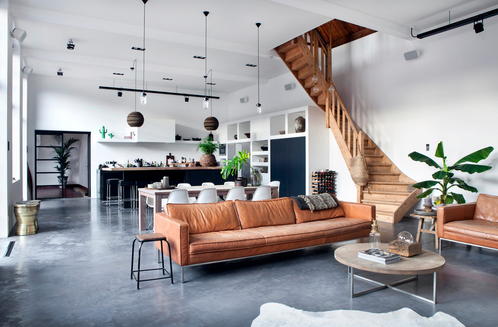 Photo of a large industrial enclosed living room in Amsterdam with a music area, concrete floors, a wall-mounted tv, white walls and grey floor.