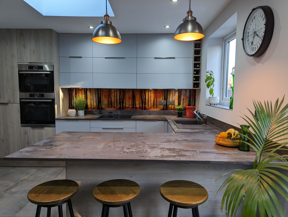 Inspiration for a medium sized urban u-shaped kitchen/diner in London with flat-panel cabinets, grey cabinets, composite countertops, multi-coloured splashback, glass sheet splashback, black appliances, porcelain flooring, grey worktops and a feature wall.