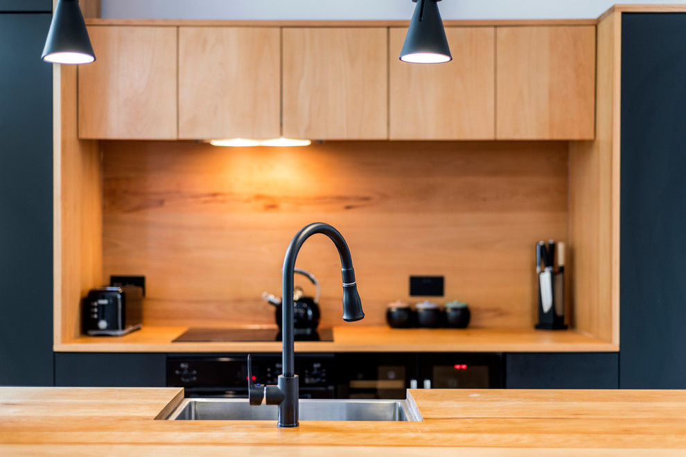 Photo of a small contemporary galley open plan kitchen in London with a farmhouse sink, flat-panel cabinets, black cabinets, wood benchtops, black appliances, porcelain floors and with island.