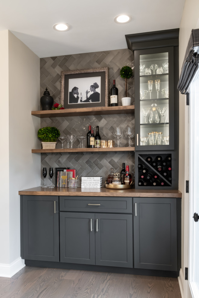 Inspiration for a small transitional single-wall home bar in St Louis with no sink, recessed-panel cabinets, grey cabinets, wood benchtops, grey splashback, ceramic splashback, medium hardwood floors, brown floor and brown benchtop.