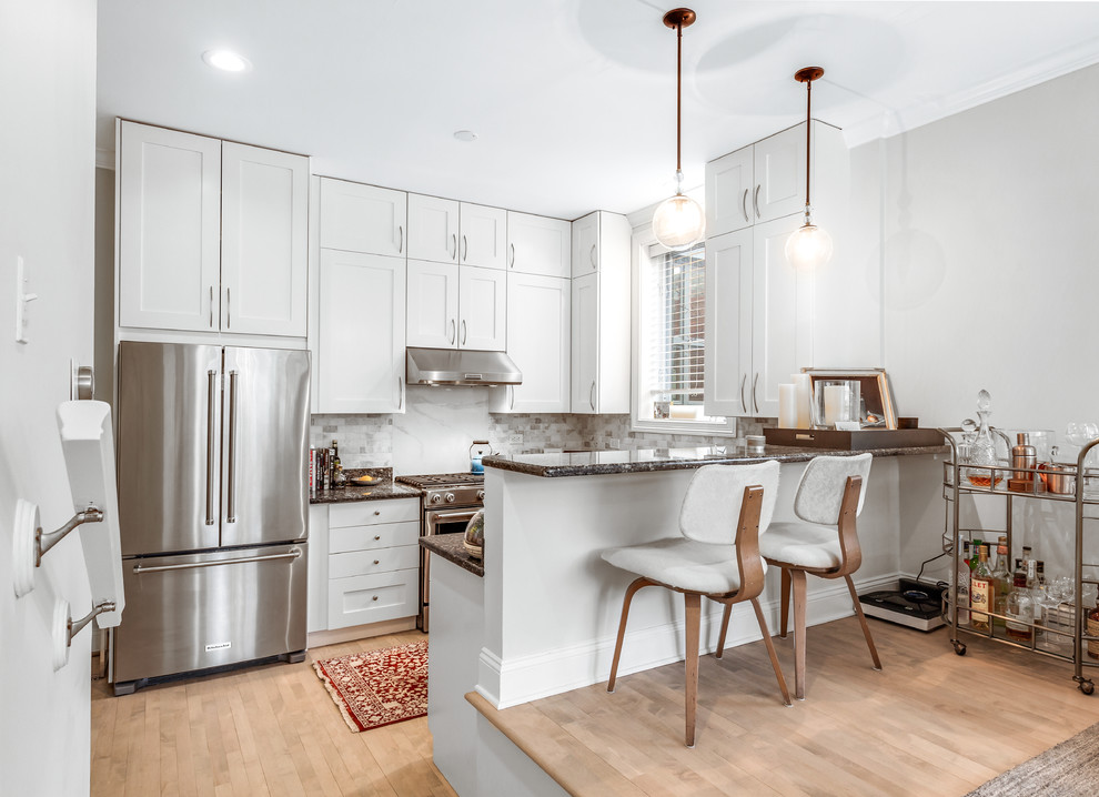 Inspiration for a mid-sized transitional u-shaped kitchen in Chicago with an undermount sink, shaker cabinets, white cabinets, granite benchtops, ceramic splashback, stainless steel appliances, grey splashback, light hardwood floors and a peninsula.