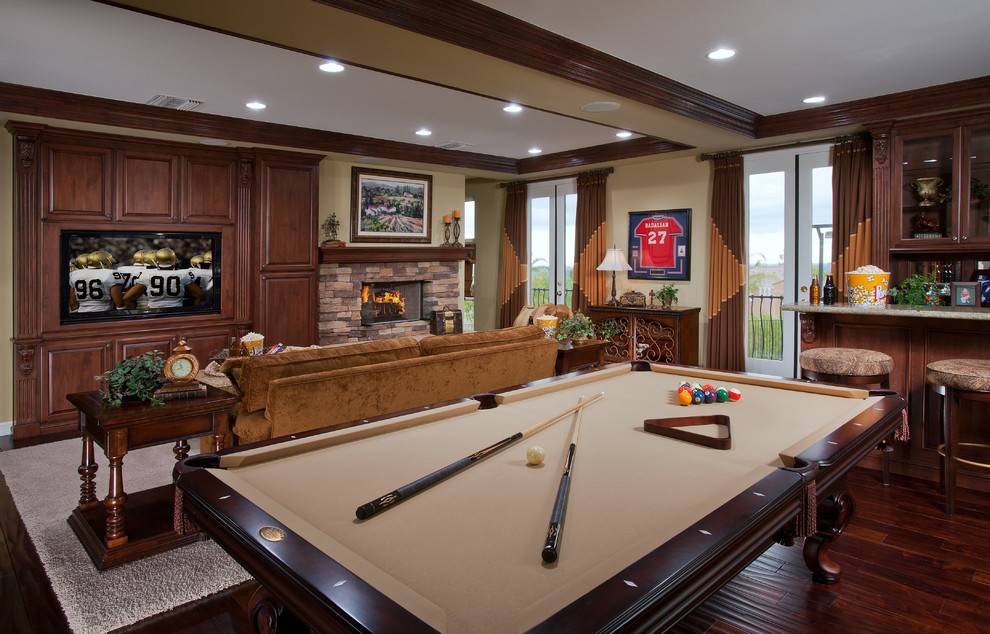 Large traditional open concept family room in Orange County with a game room, beige walls, vinyl floors, a standard fireplace, a stone fireplace surround, a built-in media wall and brown floor.