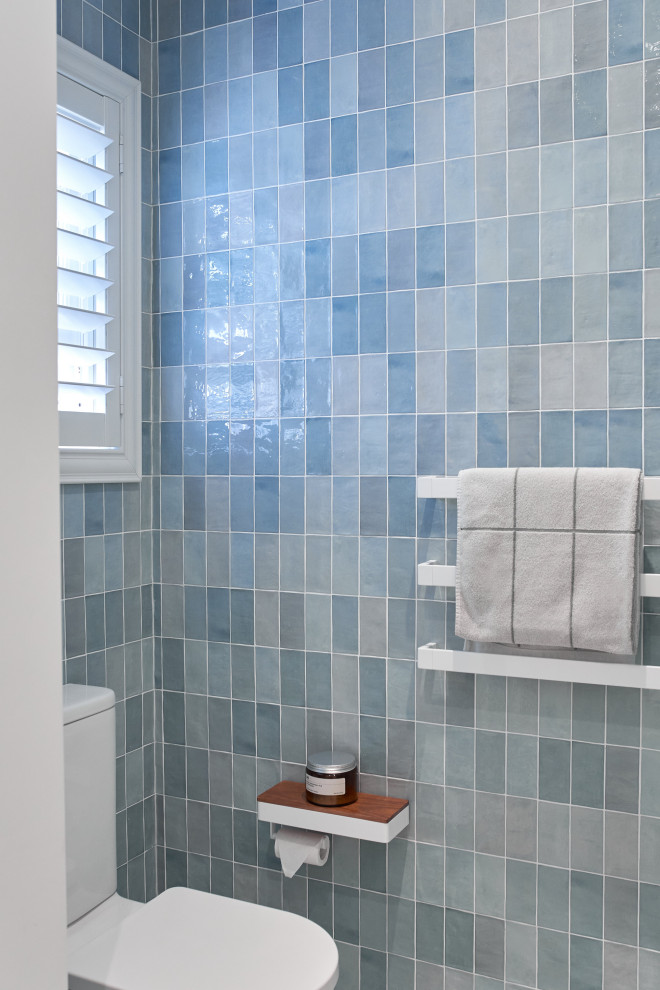 This is an example of a mid-sized contemporary bathroom in Sydney with shaker cabinets, white cabinets, an alcove shower, a one-piece toilet, blue tile, ceramic tile, white walls, porcelain floors, a vessel sink, engineered quartz benchtops, beige floor, a hinged shower door, white benchtops, a single vanity, a built-in vanity and panelled walls.