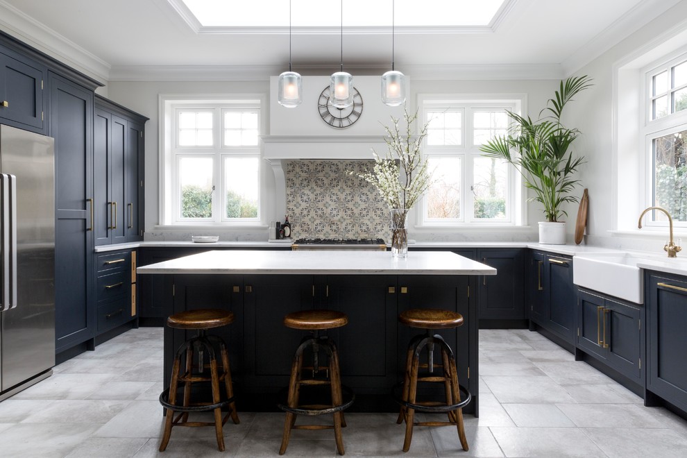 Design ideas for a large transitional u-shaped kitchen in Surrey with a farmhouse sink, blue cabinets, stainless steel appliances, with island, grey floor, white benchtop, shaker cabinets, beige splashback and mosaic tile splashback.