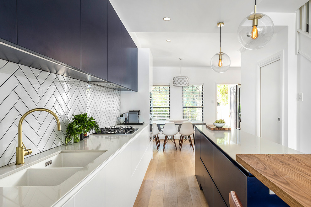 Large contemporary galley open plan kitchen in Sydney with an undermount sink, flat-panel cabinets, blue cabinets, quartz benchtops, white splashback, subway tile splashback, stainless steel appliances, light hardwood floors, with island, brown floor and white benchtop.