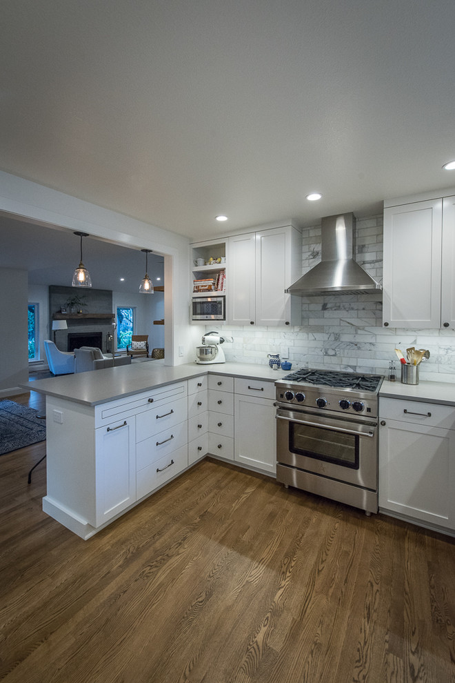 Example of a transitional u-shaped medium tone wood floor kitchen design with shaker cabinets, white cabinets, gray backsplash, stainless steel appliances and an undermount sink