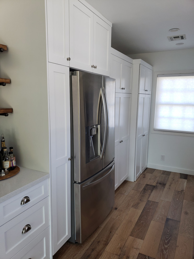 Foto på ett retro vit kök, med en dubbel diskho, skåp i shakerstil, vita skåp, bänkskiva i kvarts, grått stänkskydd, stänkskydd i keramik, rostfria vitvaror, ljust trägolv och brunt golv