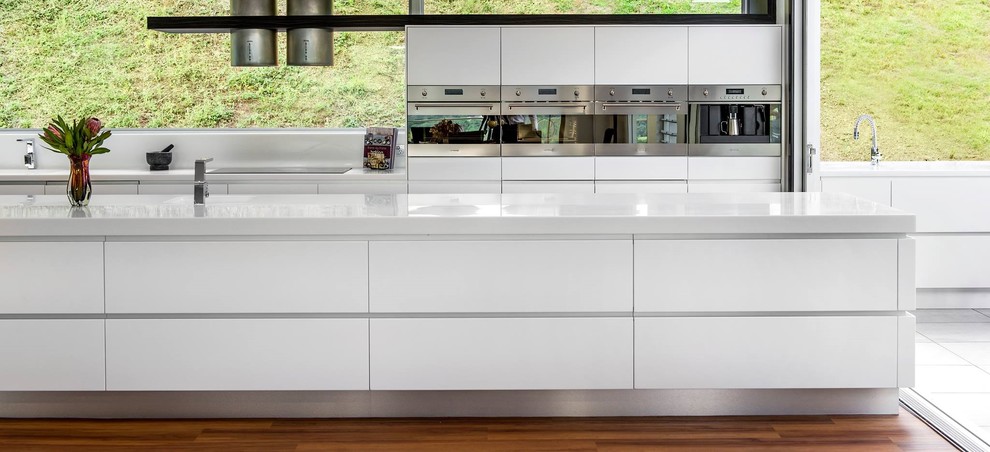 Design ideas for a large contemporary galley eat-in kitchen in Brisbane with flat-panel cabinets, white cabinets, solid surface benchtops, red splashback, glass sheet splashback, medium hardwood floors and with island.