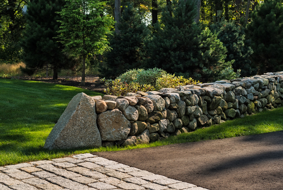 Photo of a large beach style front yard partial sun driveway in Boston with a retaining wall and natural stone pavers.
