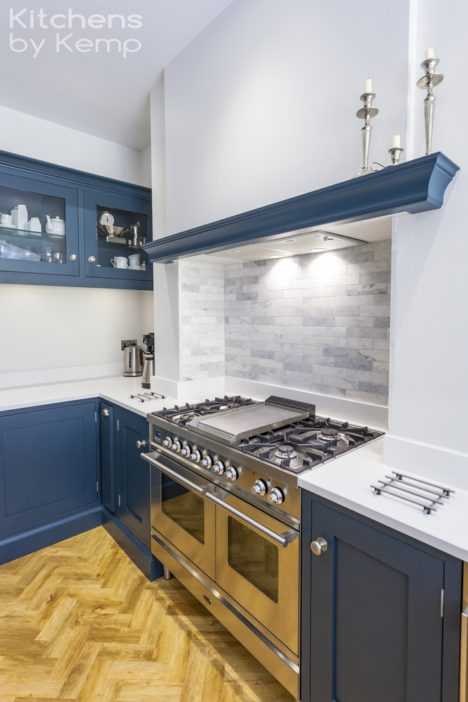 This is an example of a mid-sized transitional u-shaped open plan kitchen in Cheshire with a single-bowl sink, blue cabinets, quartzite benchtops, blue splashback, marble splashback, stainless steel appliances, vinyl floors, a peninsula, white benchtop and shaker cabinets.