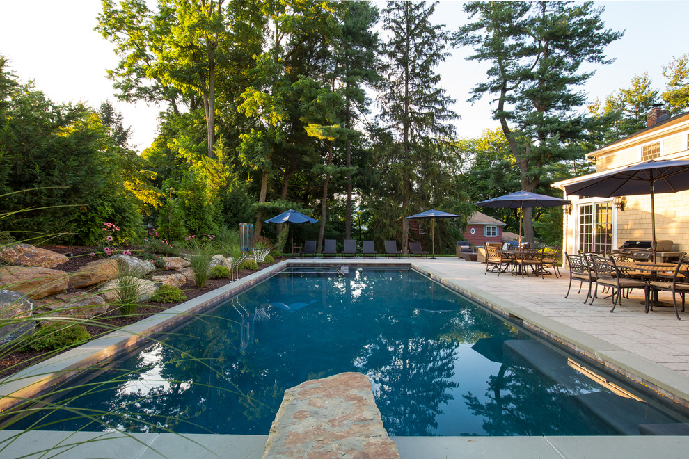 This is an example of a large traditional backyard rectangular lap pool in New York with a hot tub and natural stone pavers.