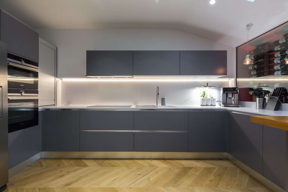 Large contemporary l-shaped eat-in kitchen in Nice with an undermount sink, grey cabinets, solid surface benchtops, white splashback, limestone splashback, panelled appliances, light hardwood floors and no island.
