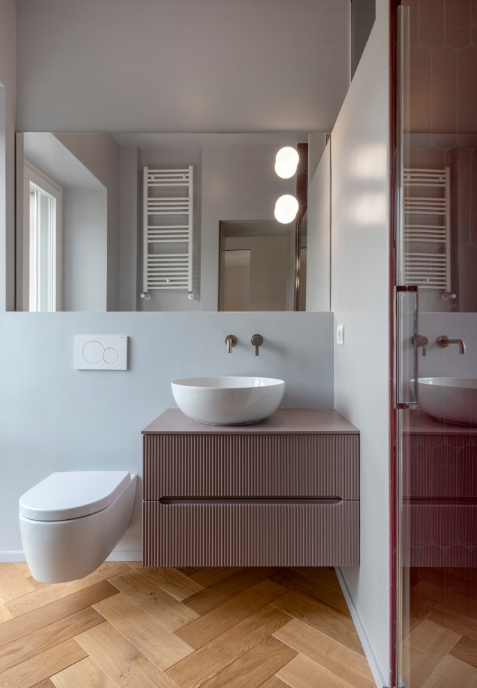 Idéer för att renovera ett mellanstort funkis lila lila badrum med dusch, med luckor med upphöjd panel, lila skåp, en dusch i en alkov, en vägghängd toalettstol, rosa kakel, porslinskakel, grå väggar, mellanmörkt trägolv, ett fristående handfat, träbänkskiva och dusch med gångjärnsdörr