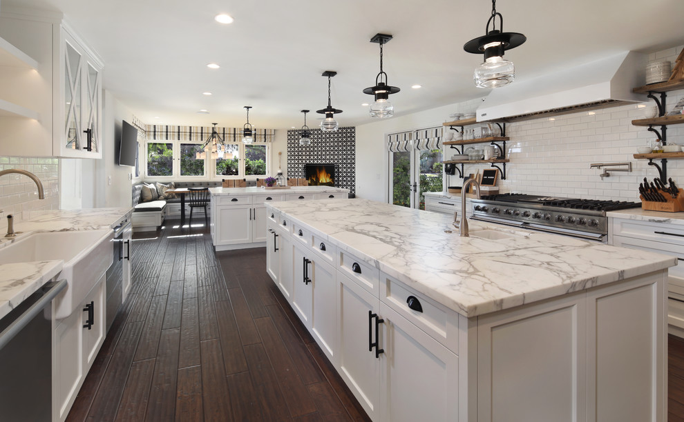 Inspiration for a country u-shaped eat-in kitchen in Orange County with a farmhouse sink, shaker cabinets, white cabinets, quartz benchtops, white splashback, subway tile splashback, stainless steel appliances, dark hardwood floors, multiple islands and brown floor.
